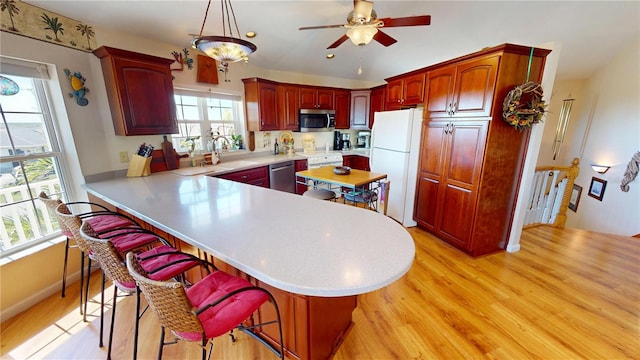 kitchen featuring appliances with stainless steel finishes, a peninsula, light countertops, light wood-type flooring, and a kitchen bar