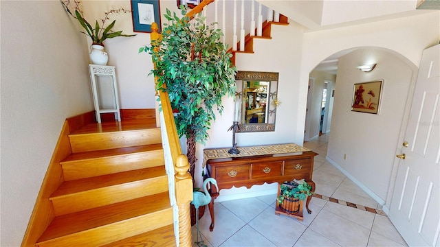 tiled entryway featuring arched walkways, stairway, and baseboards