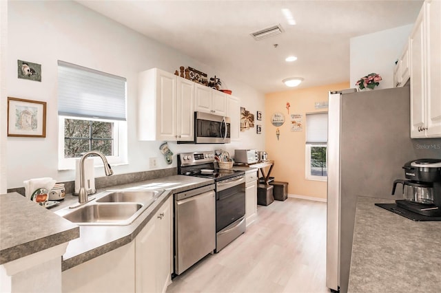 kitchen featuring light wood-style flooring, stainless steel appliances, a sink, visible vents, and white cabinets