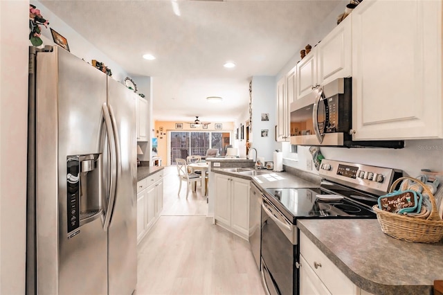 kitchen featuring dark countertops, appliances with stainless steel finishes, white cabinetry, a sink, and a peninsula