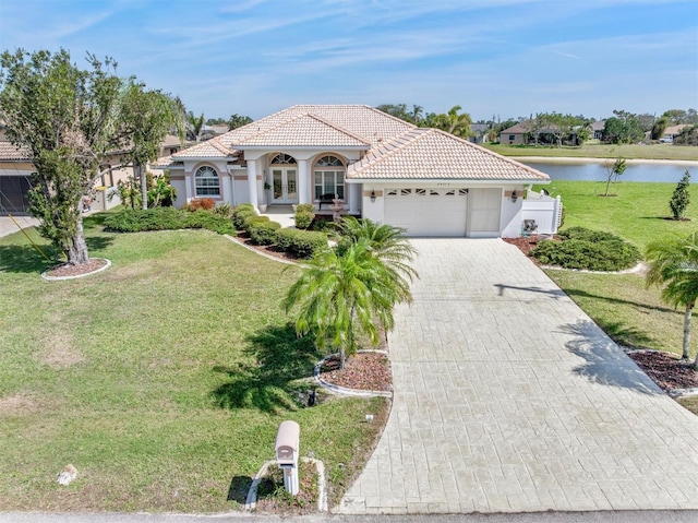 mediterranean / spanish home with an attached garage, a water view, a tiled roof, decorative driveway, and a front yard