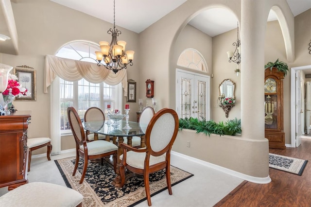 dining room with arched walkways, high vaulted ceiling, wood finished floors, baseboards, and an inviting chandelier