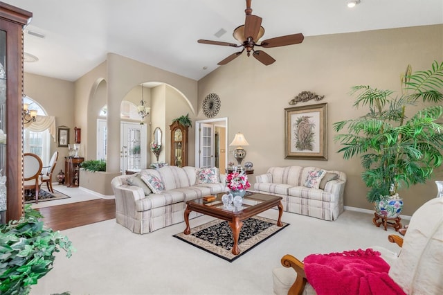 living room featuring high vaulted ceiling, arched walkways, baseboards, and ceiling fan with notable chandelier