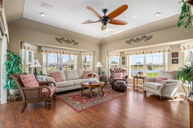 living room featuring ceiling fan, visible vents, baseboards, vaulted ceiling, and dark wood finished floors