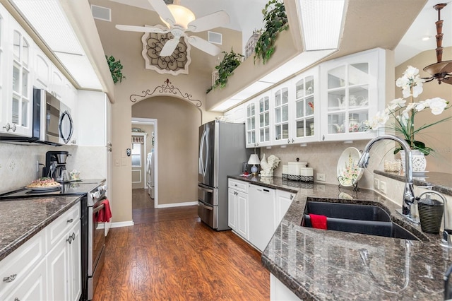 kitchen featuring appliances with stainless steel finishes, glass insert cabinets, white cabinetry, a sink, and dark stone counters