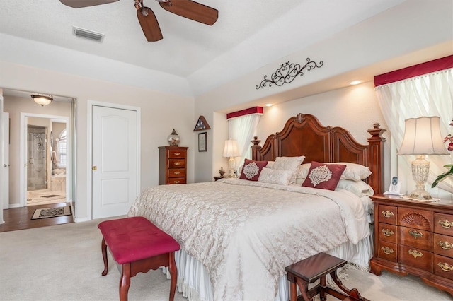 carpeted bedroom featuring ensuite bathroom, a tray ceiling, visible vents, and a ceiling fan