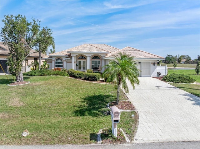 mediterranean / spanish-style home with decorative driveway, stucco siding, a front yard, a garage, and a tiled roof