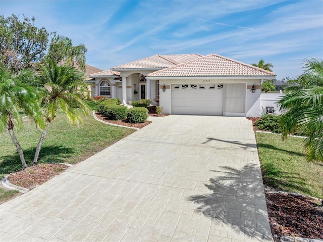 mediterranean / spanish home with a garage, decorative driveway, a tiled roof, and stucco siding