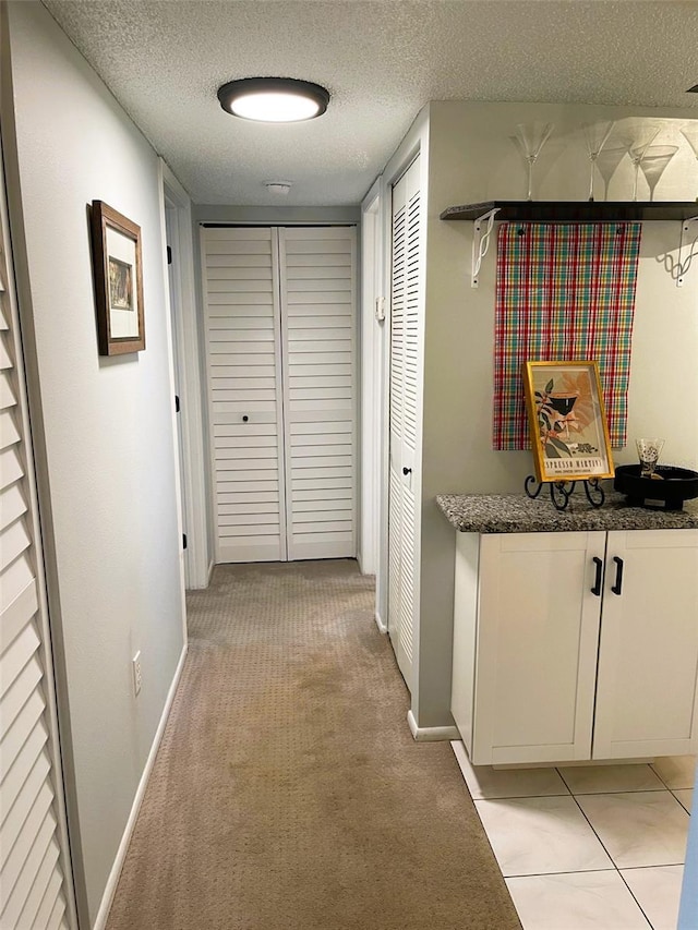 hall with light colored carpet, a textured ceiling, and baseboards