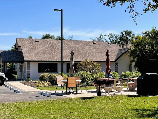 back of property with a yard, a shingled roof, a patio area, and stucco siding