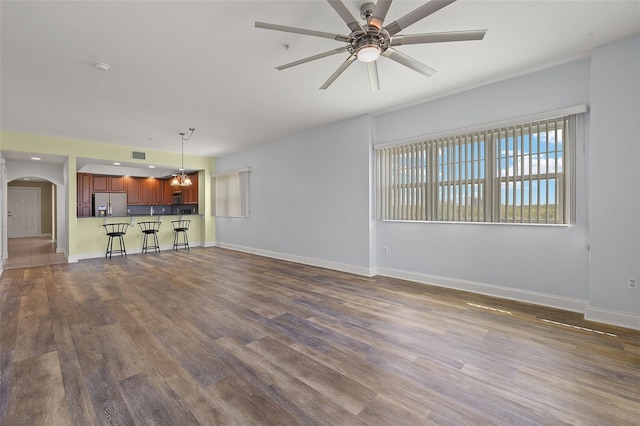 unfurnished living room with baseboards, arched walkways, dark wood-type flooring, and ceiling fan