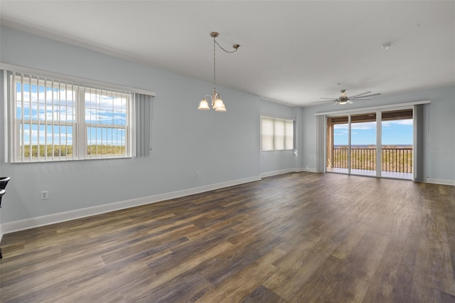 empty room featuring dark wood-style floors, ceiling fan with notable chandelier, and baseboards