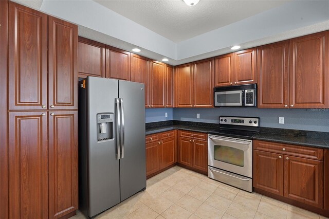 kitchen featuring dark stone countertops, light tile patterned floors, recessed lighting, appliances with stainless steel finishes, and brown cabinets