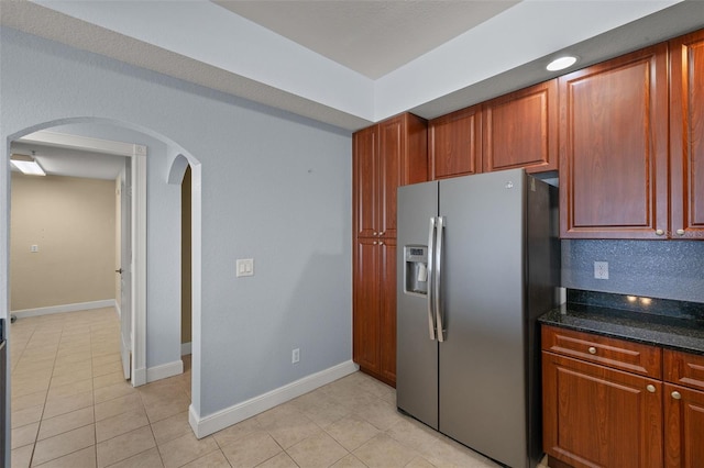 kitchen with baseboards, arched walkways, light tile patterned flooring, and stainless steel fridge with ice dispenser