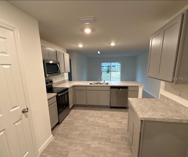 kitchen featuring stainless steel appliances, light countertops, gray cabinetry, a sink, and a peninsula