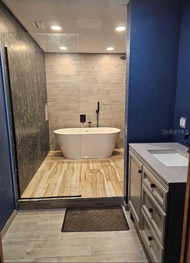 bathroom with vanity, a bathtub, and tile walls