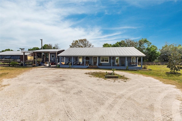 ranch-style home featuring a porch, a front yard, metal roof, and dirt driveway