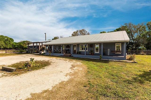 ranch-style home featuring driveway, metal roof, covered porch, fence, and a front lawn