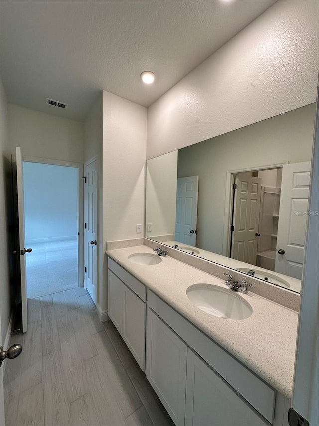 full bath with double vanity, visible vents, a sink, and wood finished floors