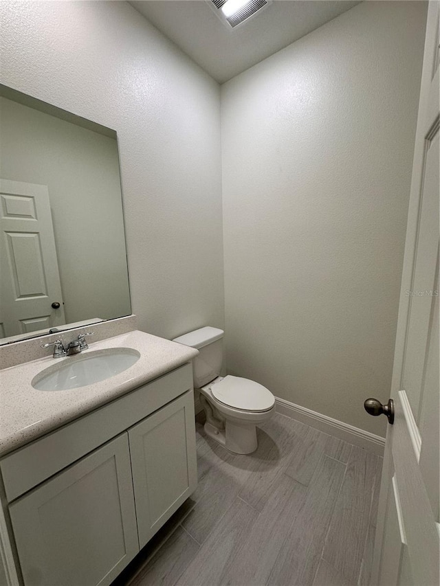 half bathroom with toilet, vanity, baseboards, visible vents, and wood tiled floor