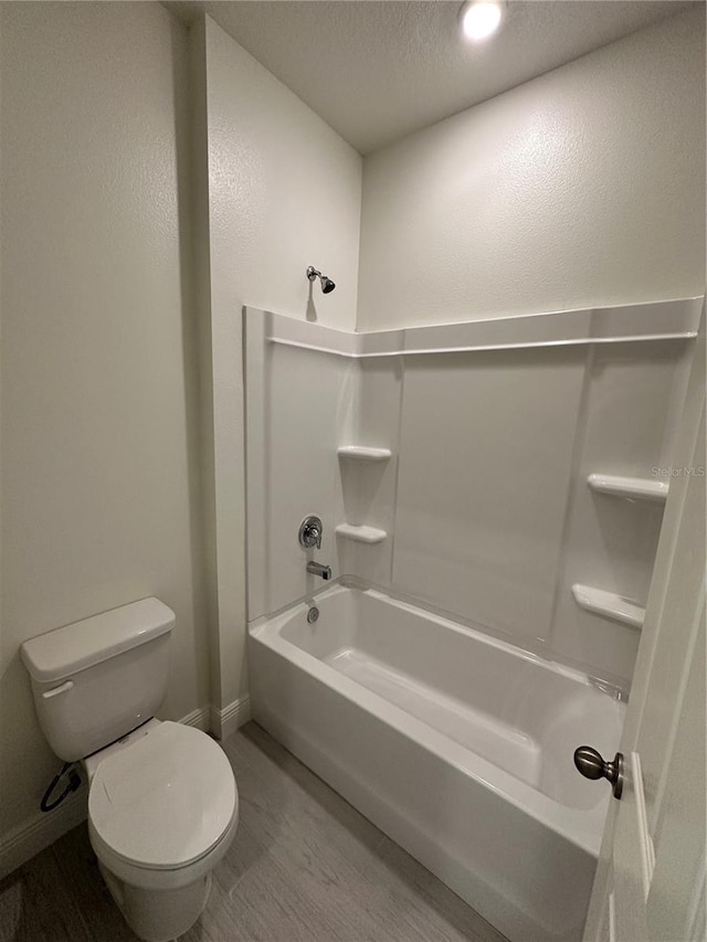 bathroom with bathtub / shower combination, toilet, a textured ceiling, wood finished floors, and baseboards