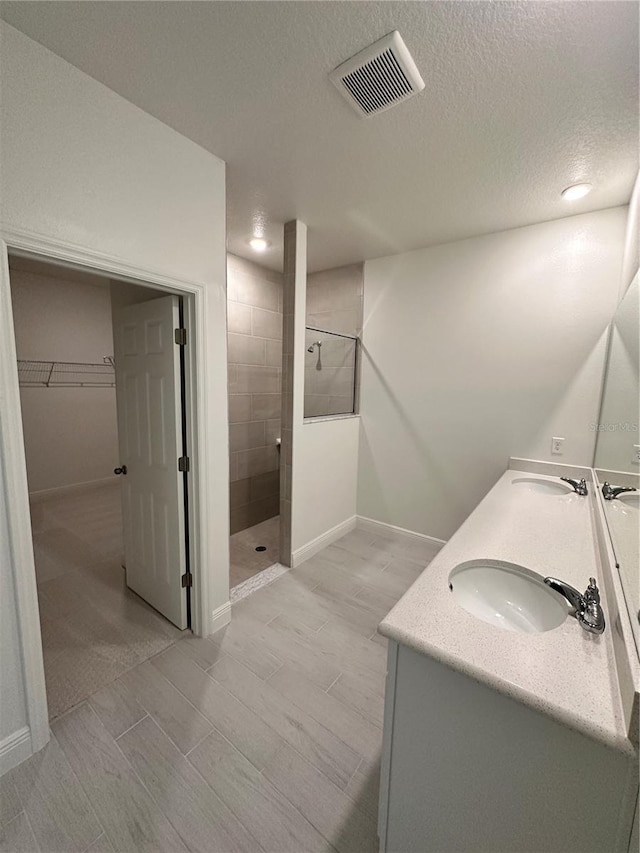 bathroom featuring double vanity, visible vents, walk in shower, and a sink