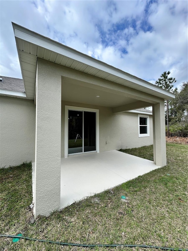 back of house featuring stucco siding, a shingled roof, a yard, and a patio