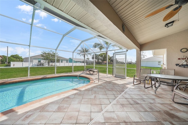 pool with a patio, a lawn, glass enclosure, fence, and ceiling fan