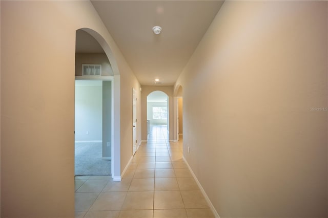 hall featuring light tile patterned floors, baseboards, visible vents, and arched walkways