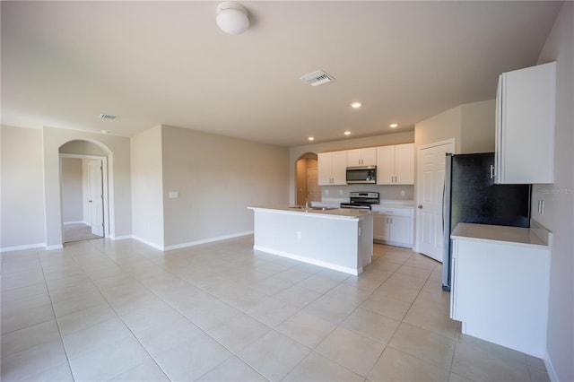 kitchen with a center island with sink, light tile patterned flooring, arched walkways, white cabinets, and stainless steel appliances