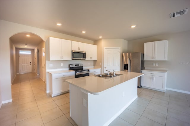 kitchen with visible vents, a kitchen island with sink, arched walkways, a sink, and stainless steel appliances