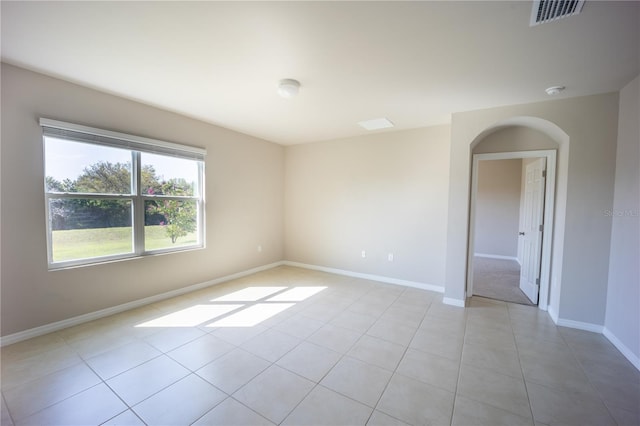 spare room with light tile patterned floors, visible vents, baseboards, and arched walkways