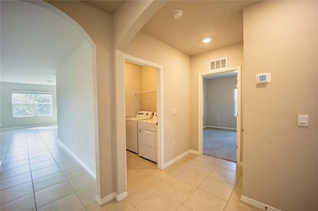 hall with baseboards, visible vents, washing machine and clothes dryer, light tile patterned flooring, and arched walkways