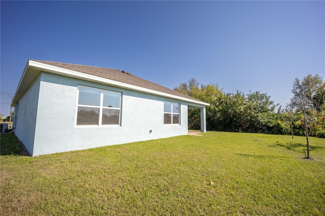 back of house with a lawn, central AC, roof with shingles, and stucco siding