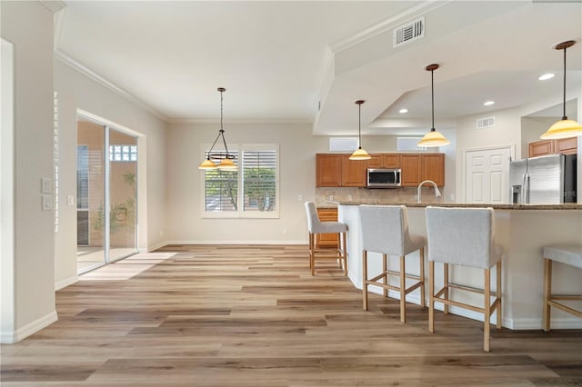 kitchen with light wood-style flooring, visible vents, a kitchen bar, light stone countertops, and stainless steel appliances