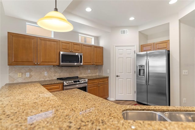 kitchen featuring hanging light fixtures, stainless steel appliances, light stone countertops, visible vents, and decorative backsplash