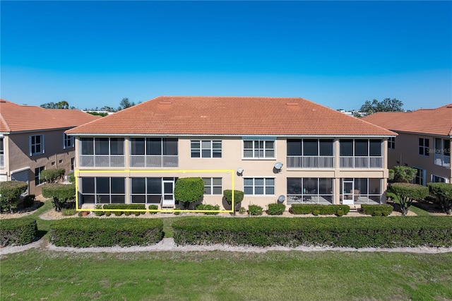 rear view of property featuring a sunroom, a lawn, and a tile roof