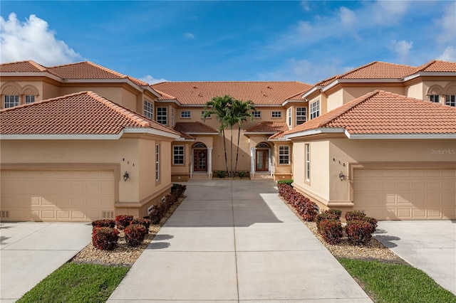 mediterranean / spanish house featuring concrete driveway, stucco siding, a tile roof, and a garage