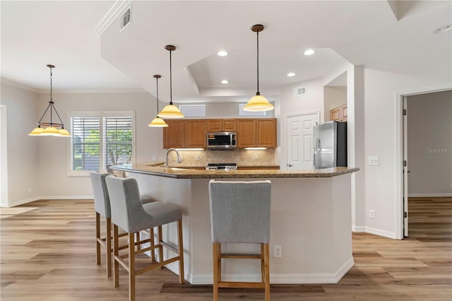 kitchen featuring brown cabinetry, hanging light fixtures, stainless steel appliances, and visible vents