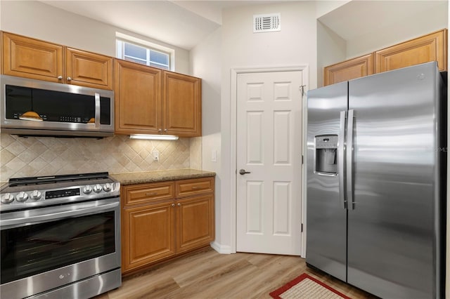 kitchen featuring light stone counters, visible vents, brown cabinets, decorative backsplash, and stainless steel appliances