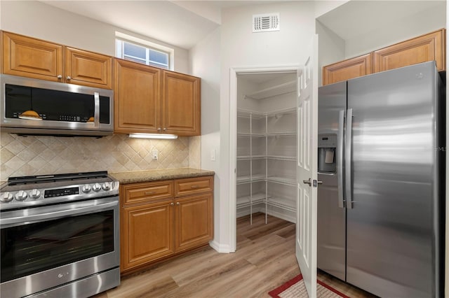 kitchen with visible vents, brown cabinets, stainless steel appliances, backsplash, and light stone countertops