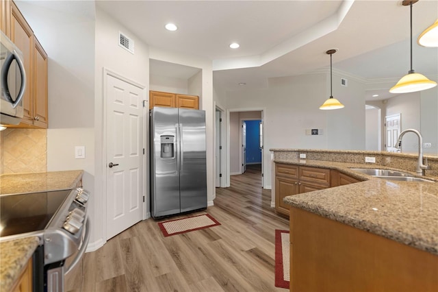 kitchen with pendant lighting, light wood-style flooring, stainless steel appliances, a sink, and backsplash