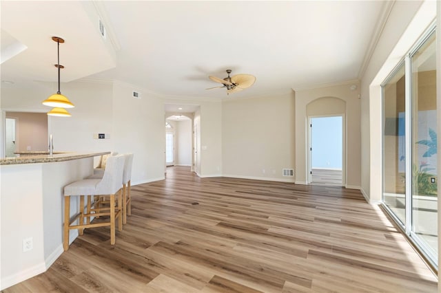 interior space featuring a ceiling fan, ornamental molding, visible vents, arched walkways, and light wood-type flooring