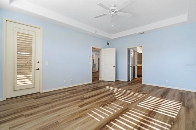 unfurnished bedroom featuring visible vents, baseboards, a raised ceiling, wood finished floors, and ensuite bathroom