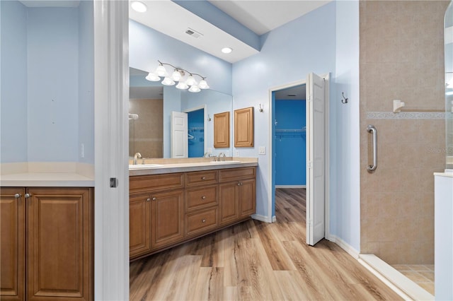 bathroom featuring double vanity, a walk in closet, visible vents, a sink, and a shower stall