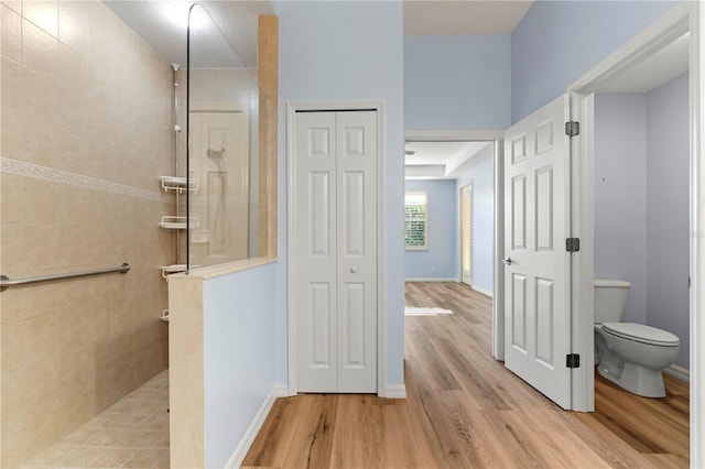 bathroom featuring wood finished floors, walk in shower, baseboards, toilet, and a closet