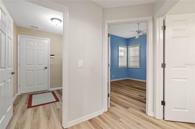 hall with baseboards, visible vents, light wood-style floors, and a textured ceiling