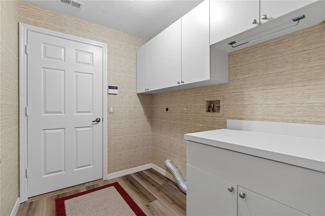 laundry area featuring baseboards, visible vents, electric dryer hookup, cabinet space, and light wood-type flooring