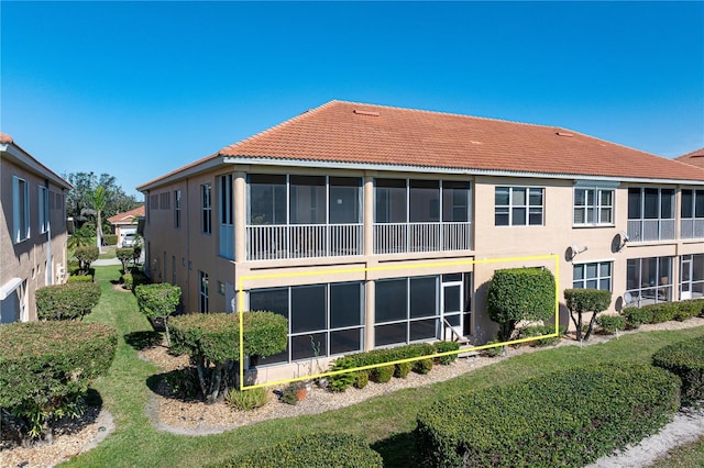 rear view of property with a tiled roof, stucco siding, a lawn, and a sunroom