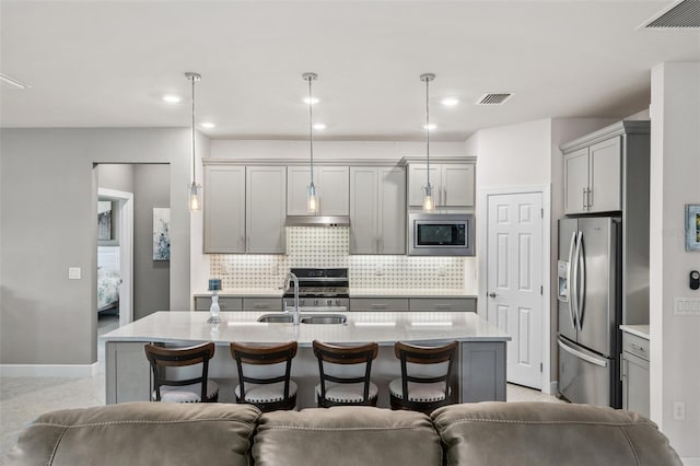 kitchen featuring an island with sink, appliances with stainless steel finishes, gray cabinetry, and decorative light fixtures